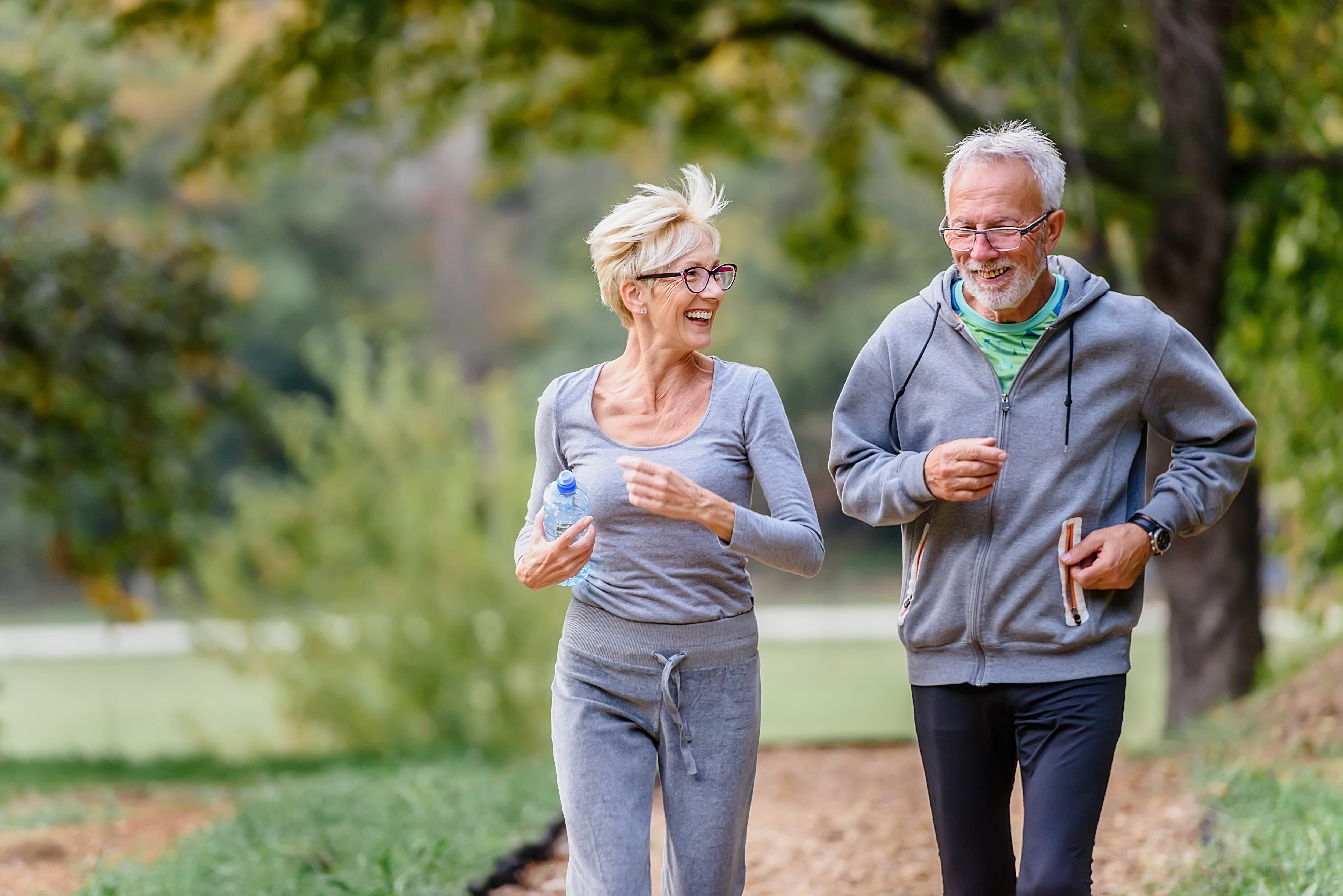 Older couple out for a run along a trail, trees blurred out in the background Older couple out for a run along a trail, trees blurred out in the background
